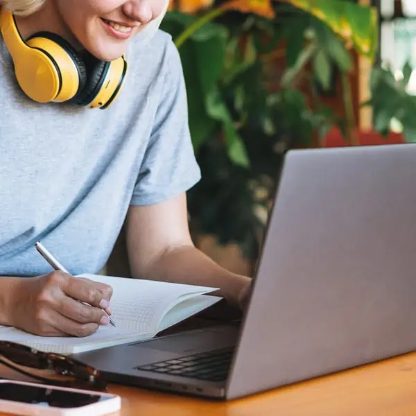 Young smiling blonde woman freelancer in with yellow headphones working on laptop on table at cafe